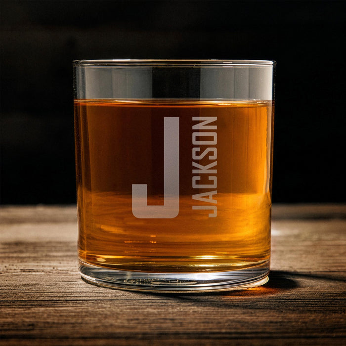 Front-facing product image of the whiskey glass on a wooden surface, clearly showing the initial and name layout for easy personalization reference.