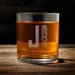 Front-facing product image of the whiskey glass on a wooden surface, clearly showing the initial and name layout for easy personalization reference.