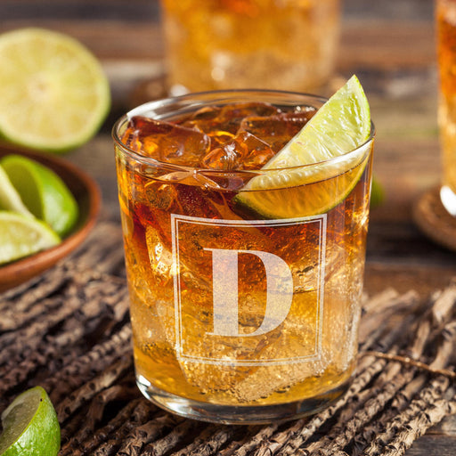 Personalized whiskey glass displayed with whiskey, ice, and fresh lime on a rustic wooden surface. The framed initial design stands out clearly, showing how the finished custom glass looks in a home bar setting.
