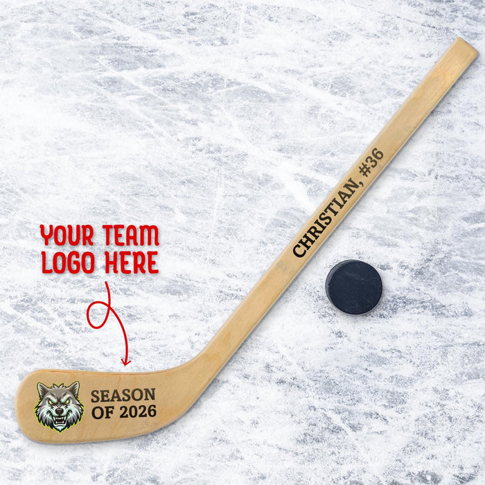 Personalized mini wooden hockey stick featuring custom team logo printed on the blade with space for team name and season text, shown on an ice background with a hockey puck.