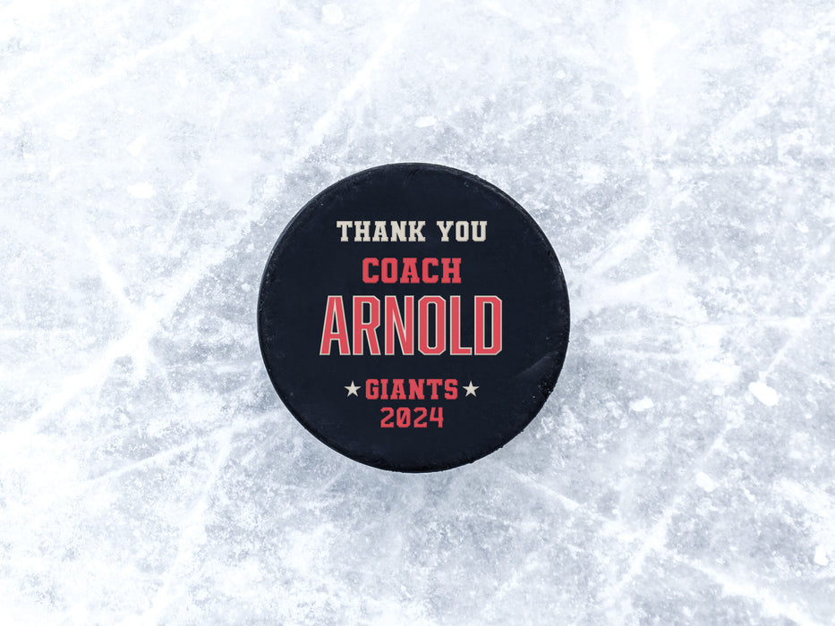 single hockey puck on blue ice rink with a red coach appreciation design that says Thank You Coach Arnold, Giants, 2024