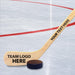 Personalized hockey stick displayed on an ice rink with “team logo here” placeholder on the blade and custom text along the handle.