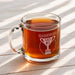 A glass mug filled with a brown liquid, likely tea, sits on a wooden surface.