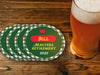 Custom round pulpboard coasters are shown sitting on a wooden table with a pint of beer beside them. The coasters read Bill Masters Retirement 2026. These feature a red, green, and yellow Masters-themed retirement party design with the retiree’s name and retirement date.