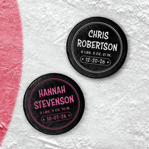 Two personalized hockey pucks with UV printed newborn birth announcement details shown in white and pink on an icy background.