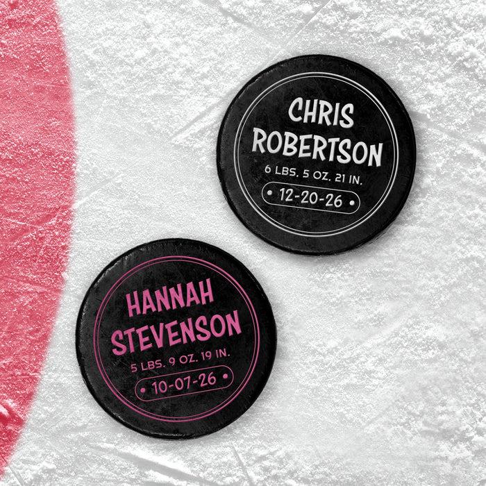 Two personalized hockey pucks with UV printed newborn birth announcement details shown in white and pink on an icy background.