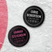 Two personalized hockey pucks with UV printed newborn birth announcement details shown in white and pink on an icy background.