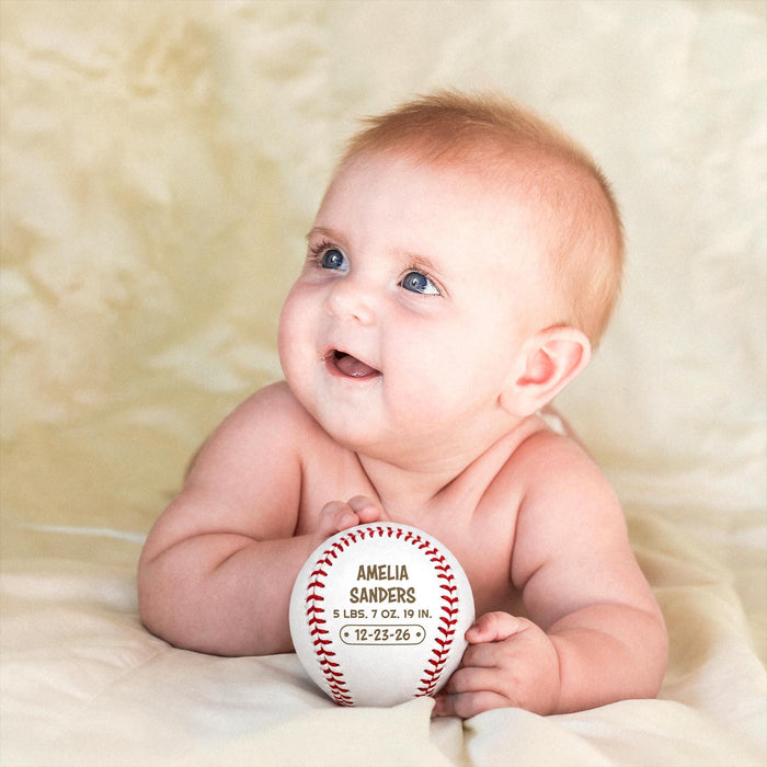 Smiling baby holding a personalized engraved baseball birth announcement with custom name, weight, length, and birth date.