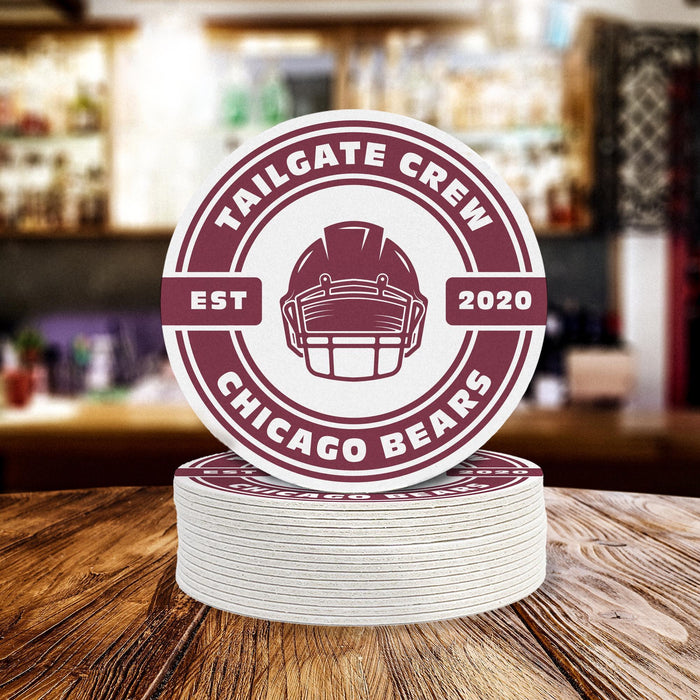 Stack of personalized Tailgate Crew football coasters featuring a helmet design, custom team name, and established year on a bar counter.