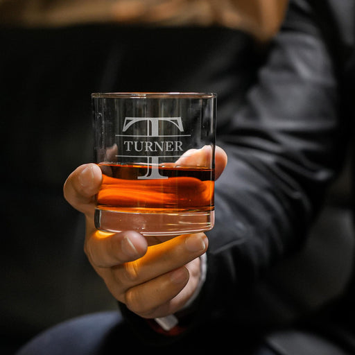 Close-up lifestyle photo of a personalized whiskey glass held in hand, featuring a large “T” initial with “Turner” engraved across the center. The glass is filled with whiskey and ice, creating a premium gift presentation.