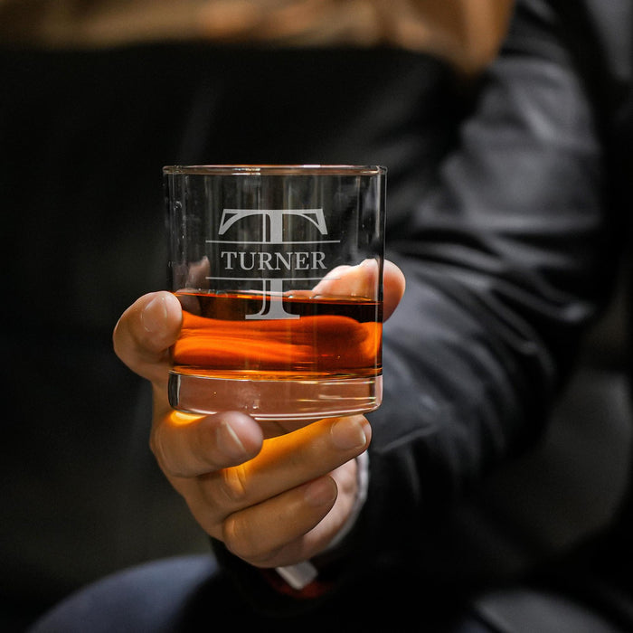 Close-up lifestyle photo of a personalized whiskey glass held in hand, featuring a large “T” initial with “Turner” engraved across the center. The glass is filled with whiskey and ice, creating a premium gift presentation.