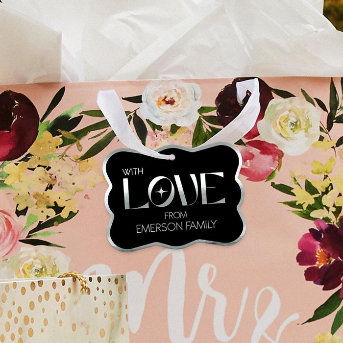 Floral wedding-themed flat lay featuring a personalized “With Love” wedding gift tag in black and metallic foil. Styled with romantic flowers and soft wedding décor accents.