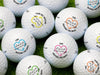 Multiple Titleist golf balls shown with different colors on each ball. Golf balls sit on a grassy surface.