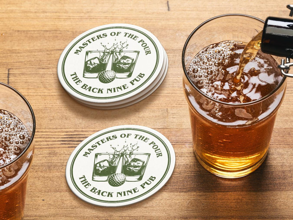 Custom round pulpboard coasters are shown sitting on a wooden table next to two drink glasses. The custom coasters feature a golf ball centered between two whiskey glasses clinking together and splashing out with customizable text wrapping around the illustration. The coaster design is printed in olive green.