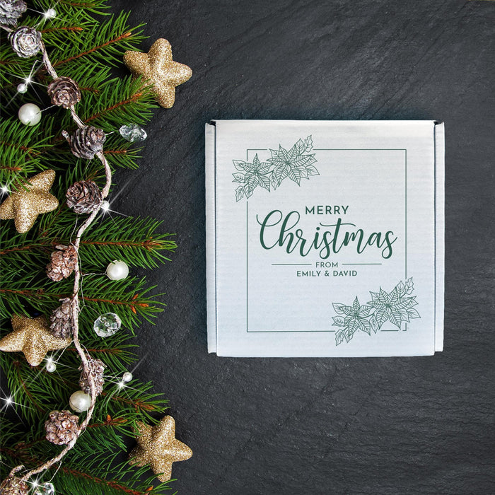 White personalized Christmas golf ball gift box beside evergreen branches and ornaments, printed with a delicate botanical Christmas design and custom name message.