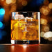 Elegant product photo of the engraved whiskey glass against a soft bokeh background. The initial and name design is centered and clearly visible.