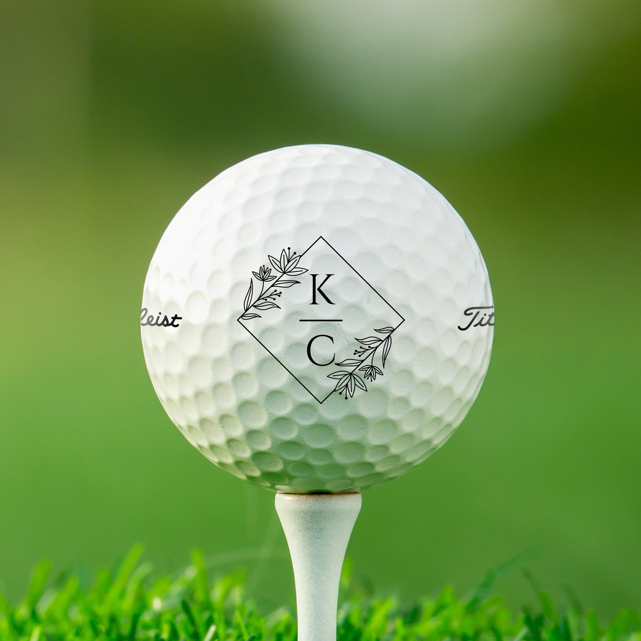 A white golf ball with a monogrammed logo on it, placed on a grassy surface.