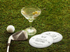 Two custom coasters sit on a grassy golf course next two a martini glass, golf club, and golf ball. The coasters feature a golf club and overlayed golf ball design with the text Members & Guests Only between stars. The last name, club name, and established year can be customized.