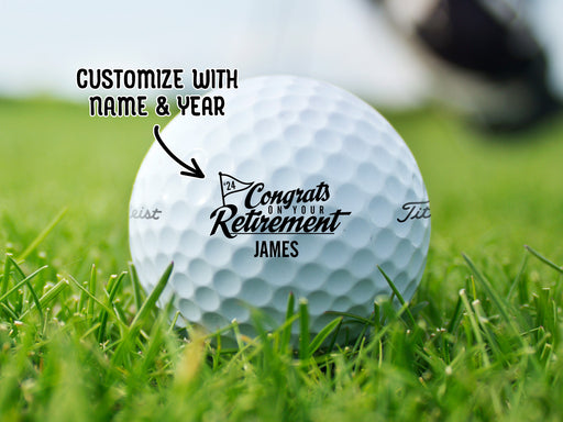 A Titleist golf ball sitting on a grassy golf course. Golf ball has Congrats On Your Retirement design on it in black. An arrow points at the ball with text that reads customize with name and year