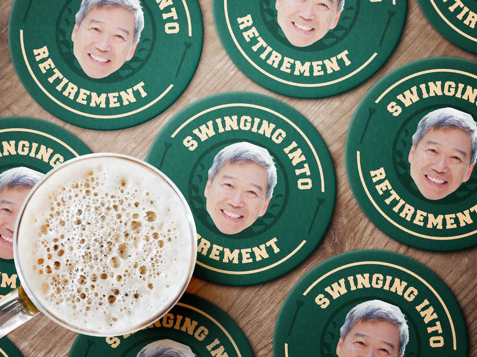Custom round pulpboard coasters are shown sitting on a wooden surface with a beer mug on top of one. The custom coasters feature design printed with playful &quot;Swinging Into Retirement&quot; text, golf imagery, and custom photo.