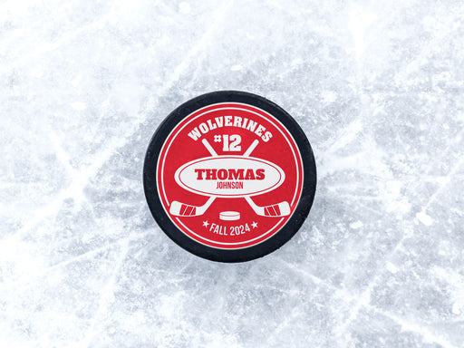hockey puck with a red player and team name design with a hockey stick design with the words Wolverines, 12, Thomas Johnson, Fall 2024