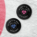 Two personalized hockey pucks with a UV printed baby birth announcement design featuring baby feet, a heart with the birth year, and custom names.