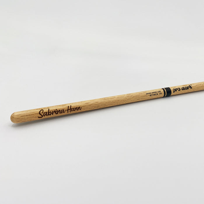 A wooden drumstick with the name Sabrina Hann engraved on it.
