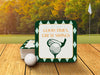 Custom square pulpboard coasters are shown on a wooden surface with golf course in the background. A gold ball is shown in front of the coasters. The coaster features design with an illustration of a golf ball and with club behind it, argyle background pattern, and custom text.