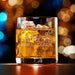Elegant product photo of the engraved whiskey glass filled with whiskey and ice against a soft bokeh background. The custom design is centered and clearly visible, perfect for showcasing the finished personalized gift.