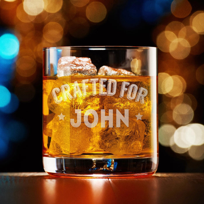 Elegant product photo of the engraved whiskey glass filled with whiskey and ice against a soft bokeh background. The custom “Crafted For John” design is centered and clearly visible, perfect for showcasing the finished personalized gift.