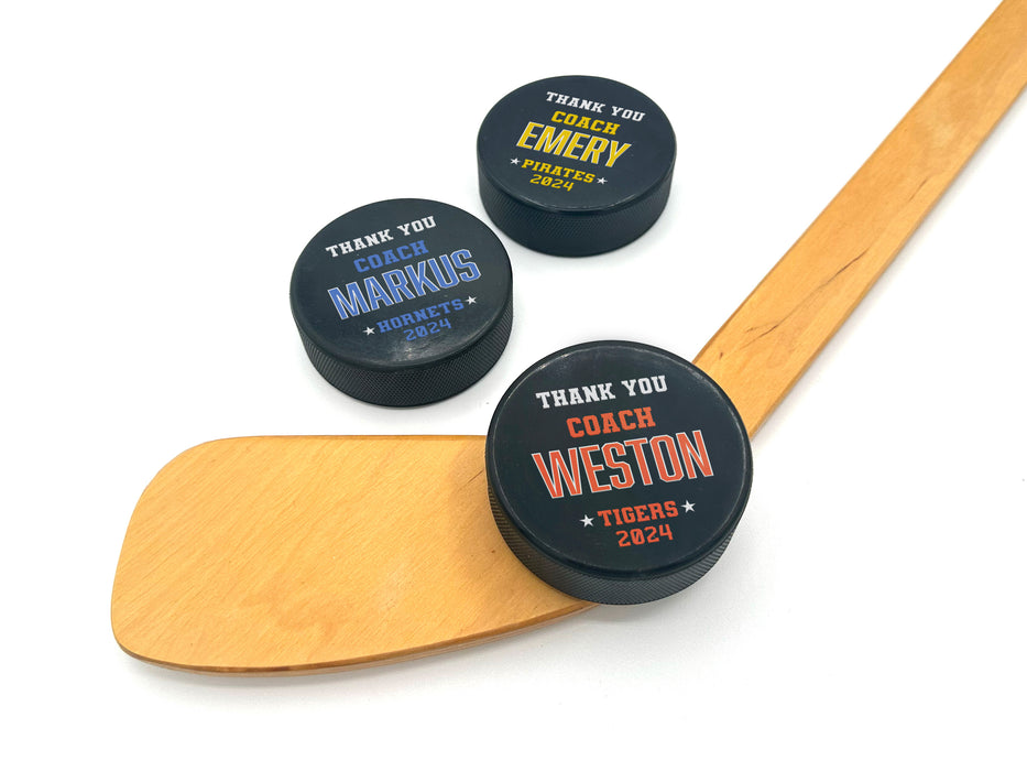 three pucks with coach appreciation designs with different names and colors on a white background with a wooden hockey stick