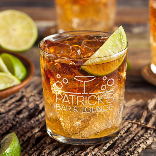 Personalized whiskey glass displayed with whiskey, ice, and fresh lime on a rustic wooden surface. The engraved “Patrick’s Bar & Lounge” design stands out clearly, showing how the finished custom rocks glass looks in a stylish bar setting.
