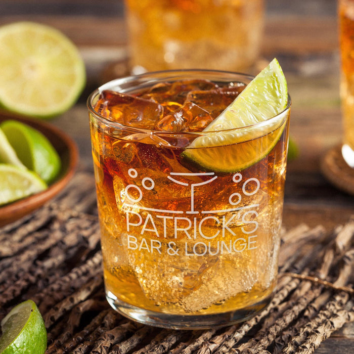 Personalized whiskey glass displayed with whiskey, ice, and fresh lime on a rustic wooden surface. The engraved “Patrick’s Bar & Lounge” design stands out clearly, showing how the finished custom rocks glass looks in a stylish bar setting.