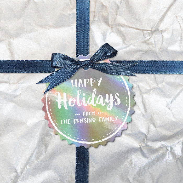 Personalized round Happy Holidays hang tag attached to a white wrapped Christmas gift with a navy ribbon and bow.
