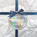 Personalized round Happy Holidays hang tag attached to a white wrapped Christmas gift with a navy ribbon and bow.