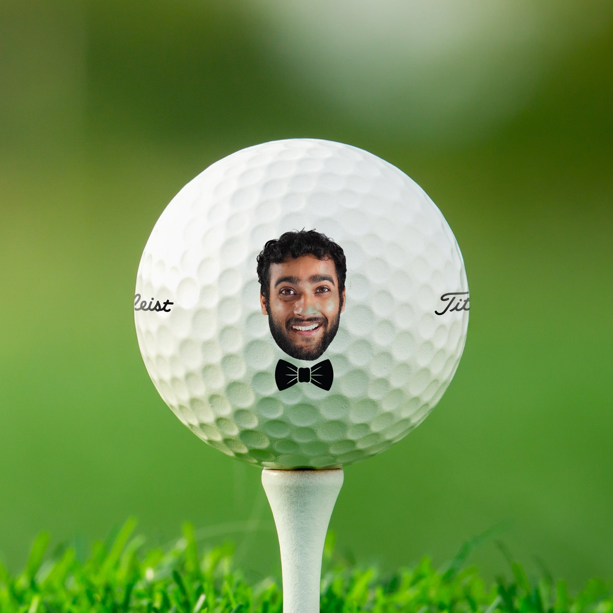A golf ball with a man's face printed on it, placed on a grassy surface.