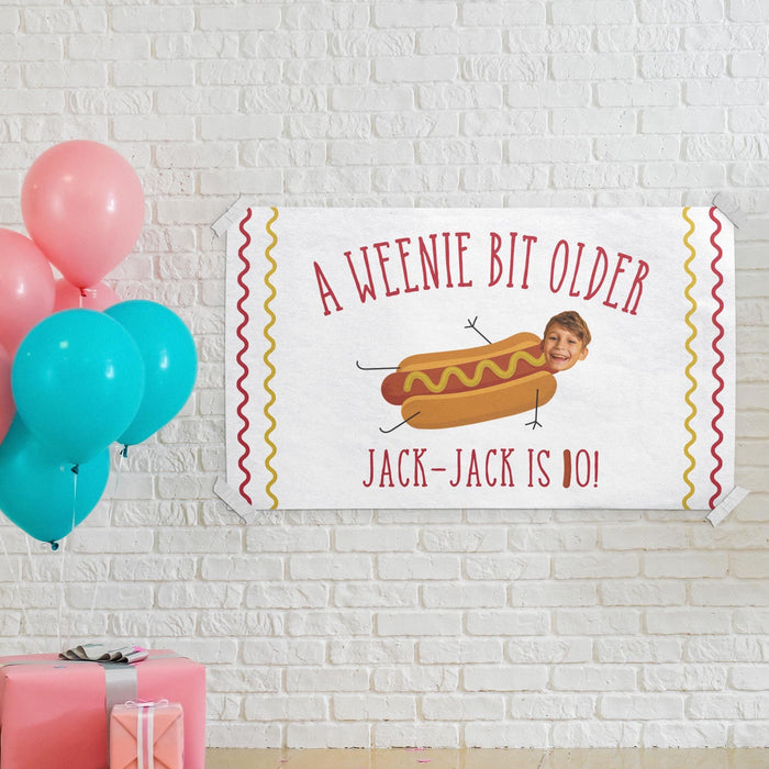 Birthday banner displayed on a white brick wall with colorful balloons and party decorations.