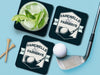 Custom square pulpboard coasters are shown sitting on a blue surface. Golf tees, a golf ball, and a golf club sit beside them. One coaster has a cocktail on top of it. The coaster features design with an illustration of a golf ball and with club behind it and custom text.