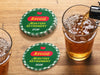 Custom round pulpboard coasters are shown sitting on a wooden table next to two drink glasses. The coasters read Reggie Masters Retirement 2025. These feature a red, green, and yellow Masters-themed retirement party design with the retiree’s name and retirement date.
