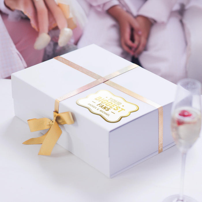 White gift box wrapped with satin ribbon and finished with a personalized gold foil “Your Biggest Fans” wedding gift tag. Elegant packaging inspiration for weddings and special occasions.