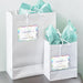 White gift bags with tissue paper featuring personalized “Let Love Sparkle” wedding gift tags in holographic rainbow foil. A modern and elegant way to personalize wedding favors and gifts.