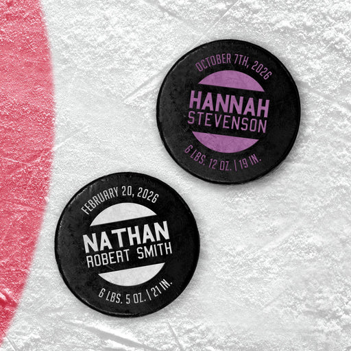 Two personalized hockey pucks with a UV printed baby birth announcement design showing custom names, dates, weight, and length in purple and white.