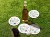 Custom round pulpboard coasters are shown sitting grass with a beer bottle, golf club, and golf ball surrounding them. The custom coasters feature design printed with green sketched cocktails with golf balls and flags within the drinks, and red and green text.