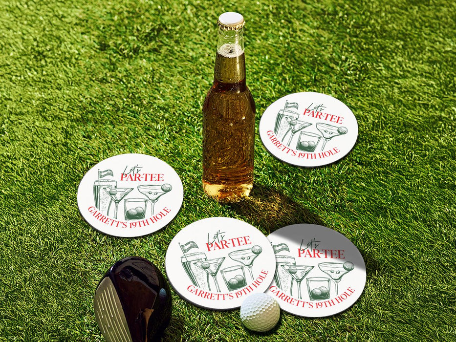 Custom round pulpboard coasters are shown sitting grass with a beer bottle, golf club, and golf ball surrounding them. The custom coasters feature design printed with green sketched cocktails with golf balls and flags within the drinks, and red and green text.