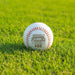 A personalized baseball with red stitching and the name "Adam Fuller" engraved on it, sitting on a grassy field.