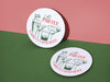 Custom round pulpboard coasters are shown sitting on a pink and green background. The custom coasters feature design printed with green sketched cocktails with golf balls and flags within the drinks, and red and green text.