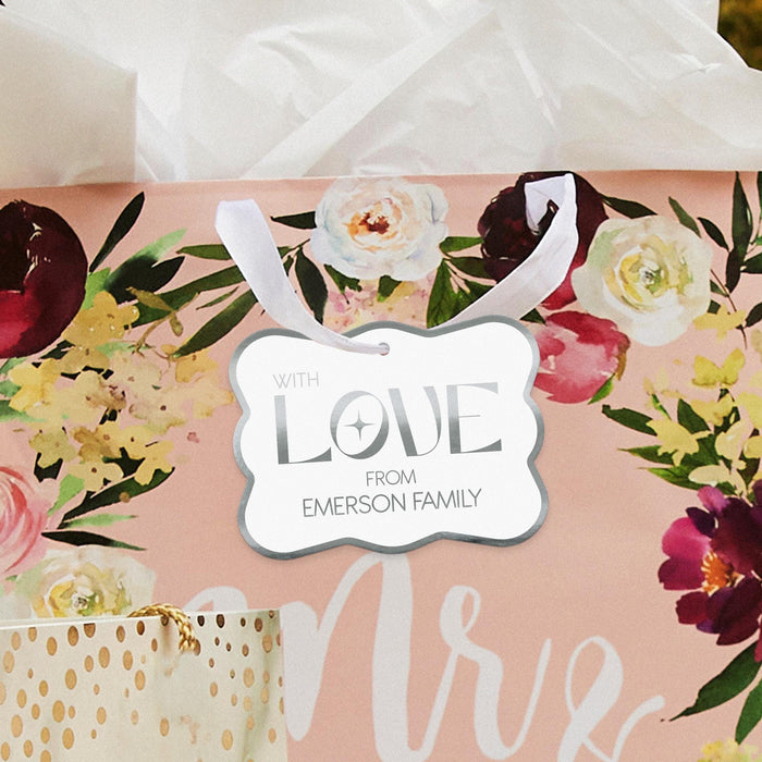 Romantic floral flat lay featuring a personalized “With Love” gift tag in metallic silver foil. Styled with flowers and soft wedding décor for bridal shower inspiration.