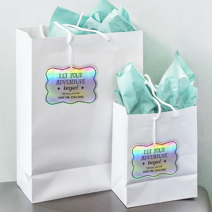 White gift bags with tissue paper decorated using personalized “Let Your Adventure Begin” holographic foil gift tags. Perfect for wedding welcome bags, favors, and bridal party gifts.