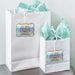 White gift bags with tissue paper decorated using personalized “Let Your Adventure Begin” holographic foil gift tags. Perfect for wedding welcome bags, favors, and bridal party gifts.