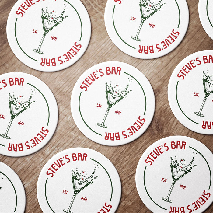 Multiple round dirty martini coasters spread across a tabletop, each featuring the personalized bar name, olive martini illustration, and established year.